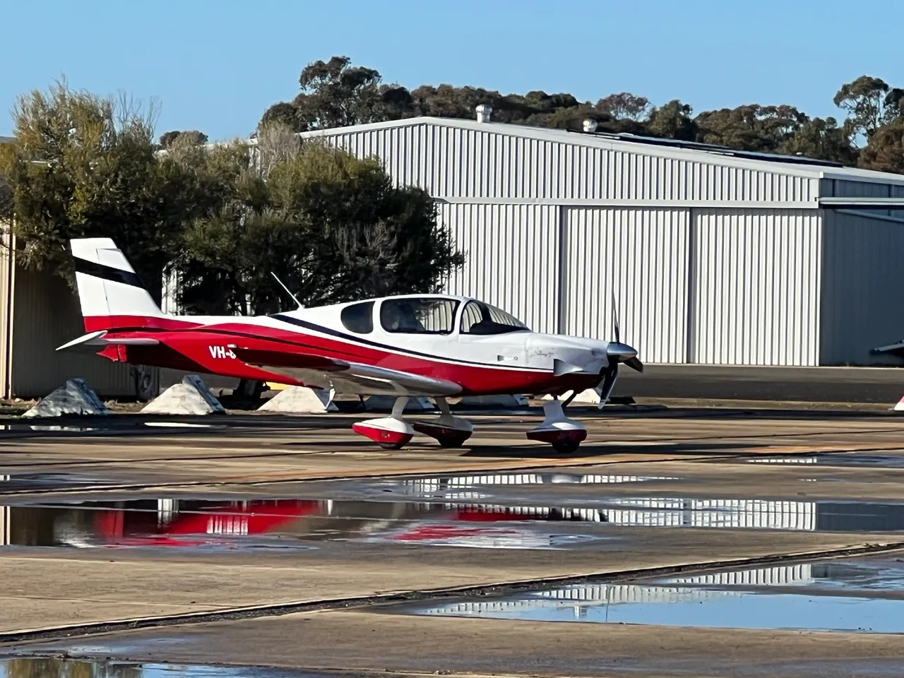 Red and white light aircraft parked outside a hangar